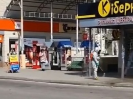 В центре Херсона днем люди в спецкостюмах дезинфицируют остановку: рядом стоят горожане в обычных масках - видео